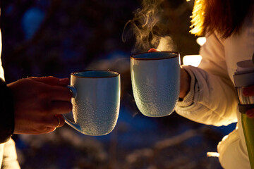 A couple warming up with hot tea in the evening winter woods in the light of car headlights