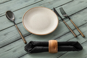 Simple table setting with plate, cutlery and napkin on color wooden background