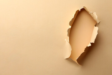 Hole in light beige paper on color background, space for text