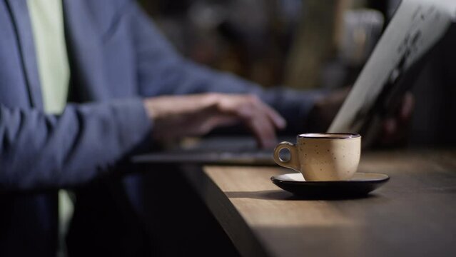 A man works at a computer in a coffee shop. Close-up of a cup of cappuccino and male hands typing on a keyboard. A businessman is working in a cafe on his lunch break. High quality 4k footage