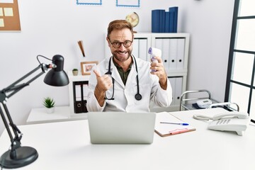 Middle age doctor man holding thermometer at the clinic smiling happy and positive, thumb up doing excellent and approval sign