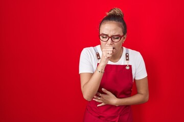 Young hispanic woman wearing waitress apron over red background feeling unwell and coughing as...