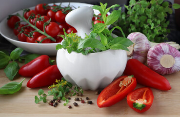 Mortar with fresh herbs near garlic, pepper and cherry tomatoes on wooden table, closeup