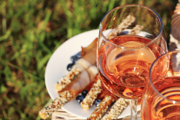 Glasses of delicious rose wine and food on wicker basket outdoors, closeup