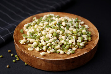 Wooden plate with sprouted green mung beans on black background, closeup