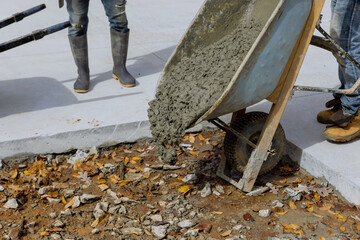 Construction worker pouring cement from wheelbarrow onto to create new sidewalk on side of house