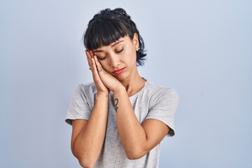Fototapeta premium Young hispanic woman wearing casual t shirt over blue background sleeping tired dreaming and posing with hands together while smiling with closed eyes.
