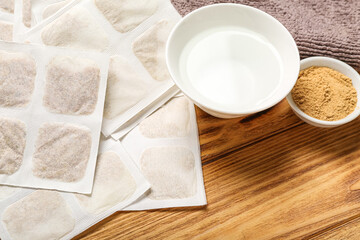 Mustard plasters with bowl of water and towel on wooden background, closeup