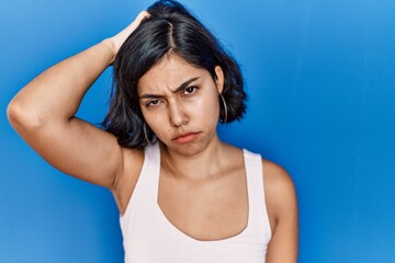 Fototapeta na wymiar Young hispanic woman standing over blue background confuse and wonder about question. uncertain with doubt, thinking with hand on head. pensive concept.