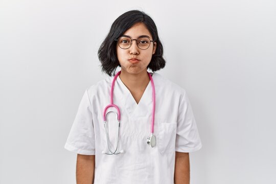 Young hispanic doctor woman wearing stethoscope over isolated background puffing cheeks with funny face. mouth inflated with air, crazy expression.