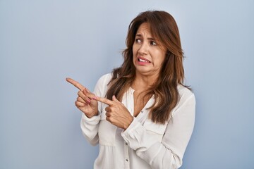 Hispanic woman standing over isolated background pointing aside worried and nervous with both hands, concerned and surprised expression