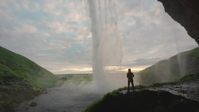 Beautiful Seljalandsfoss waterfall flowing and tourist woman standing in the cave at the evening on summer at South of Iceland