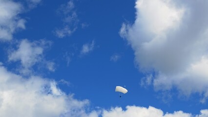 An extreme sport skydiver descends on parachute flying through clouds white wing type parachute. Thirst for adrenaline makes people jump with parachute, for adrenaline rush it causes addiction to fear