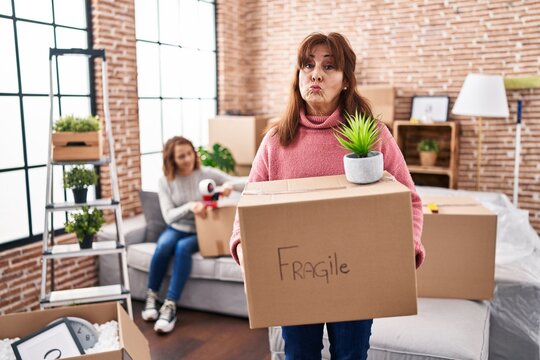 Mother and daughter moving to a new home holding cardboard box looking at the camera blowing a kiss being lovely and sexy. love expression.