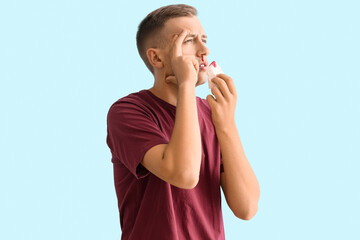 Young man with nosebleed and tissue on blue background