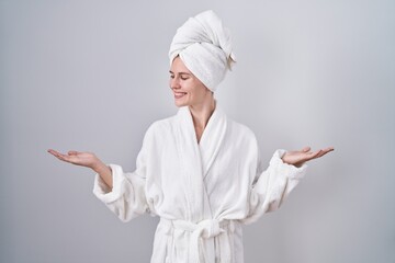 Blonde caucasian woman wearing bathrobe smiling showing both hands open palms, presenting and advertising comparison and balance - obrazy, fototapety, plakaty