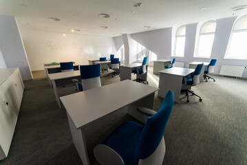 Meeting zone in the office in a loft style with white brick walls and concrete columns. Zone has a large wooden table with gray chairs and glass partitions.