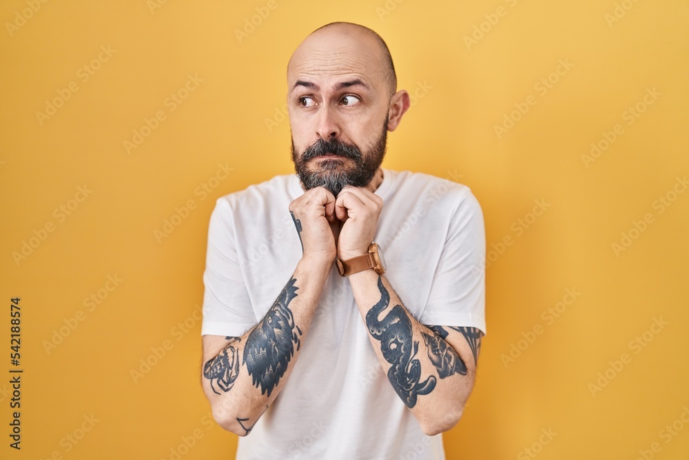 Poster young hispanic man with tattoos standing over yellow background laughing nervous and excited with ha