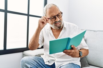 Senior grey-haired man smiling confident reading book at home