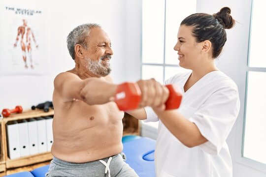Physiotherapist and patient smiling confident having rehab session using dumbbell at clinic