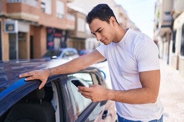 Young hispanic man using smartphone leaning on car at street
