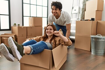 Young couple smiling happy playing with cardboard box as a car at new home.