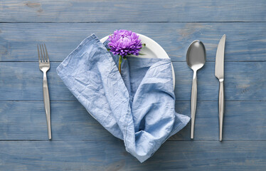 Table setting with napkin, chrysanthemum flower in plate and cutlery on blue wooden background