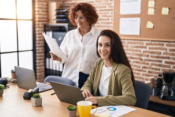 Two women business workers using laptop reading document at office