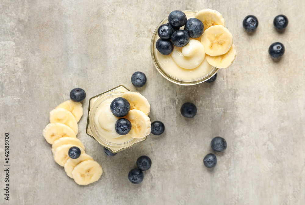 Wall mural jars of tasty vanilla pudding with banana and blueberry on light background