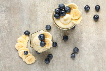 Jars of tasty vanilla pudding with banana and blueberry on light background