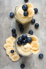 Jars of tasty vanilla pudding with banana and blueberry on light background