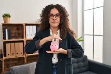 Young hispanic woman holding piggy bank relaxed with serious expression on face. simple and natural looking at the camera.