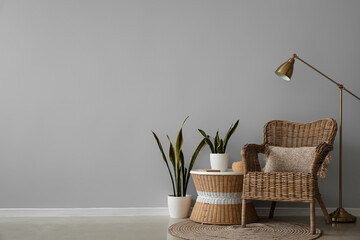 Wicker armchair, table with houseplants and lamp near grey wall