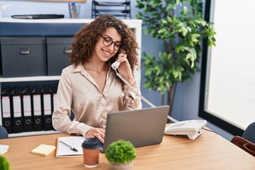 Young hispanic woman business worker using laptop talking on telephone at office