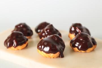 Board with delicious eclairs on white background, closeup
