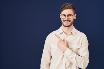 Obraz premium Hispanic man with beard standing over blue background cheerful with a smile of face pointing with hand and finger up to the side with happy and natural expression on face