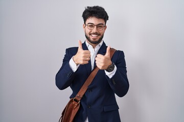 Hispanic man with beard wearing business clothes success sign doing positive gesture with hand, thumbs up smiling and happy. cheerful expression and winner gesture.
