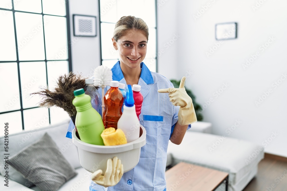 Poster young blonde woman wearing cleaner uniform holding cleaning products pointing finger to one self smi