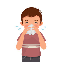 Cute little boy sneezing with flu and cold allergic symptoms blowing nose into tissue paper 