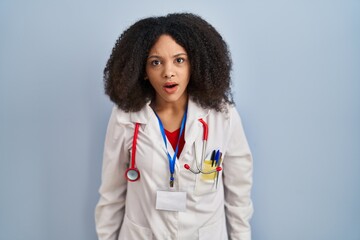 Young african american woman wearing doctor uniform and stethoscope in shock face, looking...
