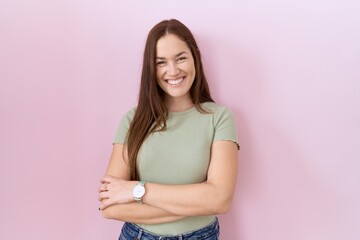 Obraz premium Beautiful brunette woman standing over pink background happy face smiling with crossed arms looking at the camera. positive person.