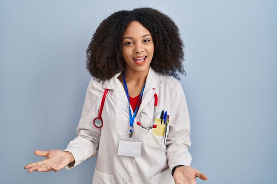 Young african american woman wearing doctor uniform and stethoscope smiling cheerful with open arms as friendly welcome, positive and confident greetings