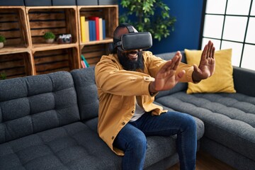 Obraz premium Young african american man playing video game using virtual reality glasses at home