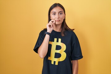 Young hispanic woman wearing bitcoin t shirt mouth and lips shut as zip with fingers. secret and...
