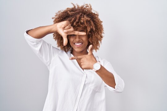 Young hispanic woman with curly hair standing over white background smiling making frame with hands and fingers with happy face. creativity and photography concept.