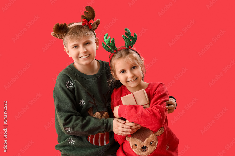 Wall mural happy little children in reindeer horns with christmas presents on red background