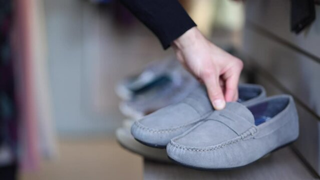 Hand of human taking gray moccasins from the shelf in clothes store. Side view
