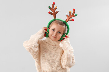 Happy little girl in reindeer horns on light background