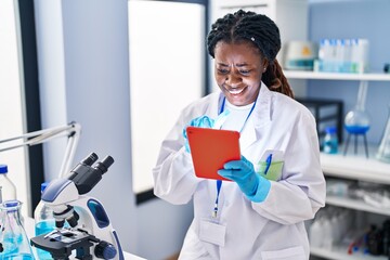 African american woman scientist smiling confident using touchpad at laboratory