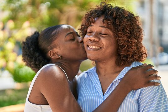 African american women mother and daughter hugging each other kissing at park